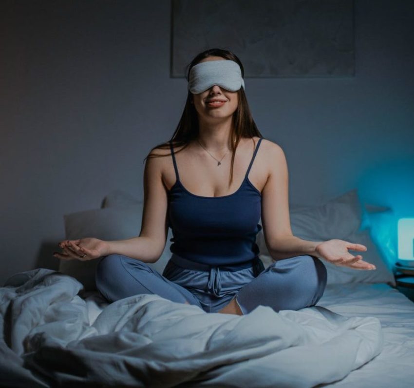 Woman Sitting Cross-Legged on Bed Wearing Sleep Mask and Meditating at Night
