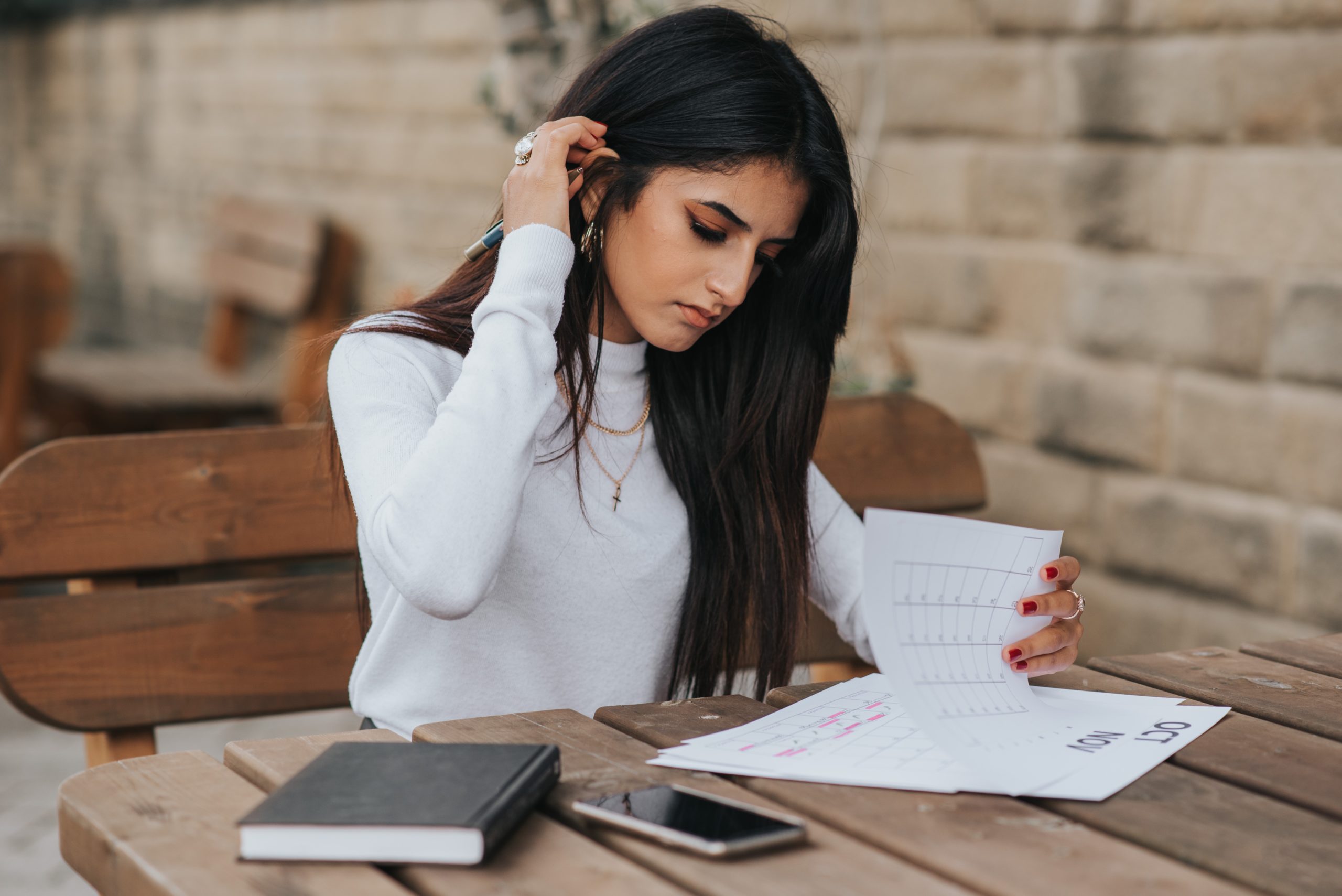 Woman Sitting at Outdoor Table Reviewing Papers With a Notebook Beside Her