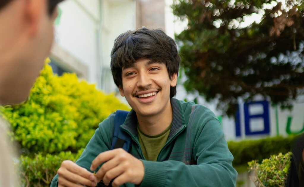 A teen sitting outside smiling at a peer.