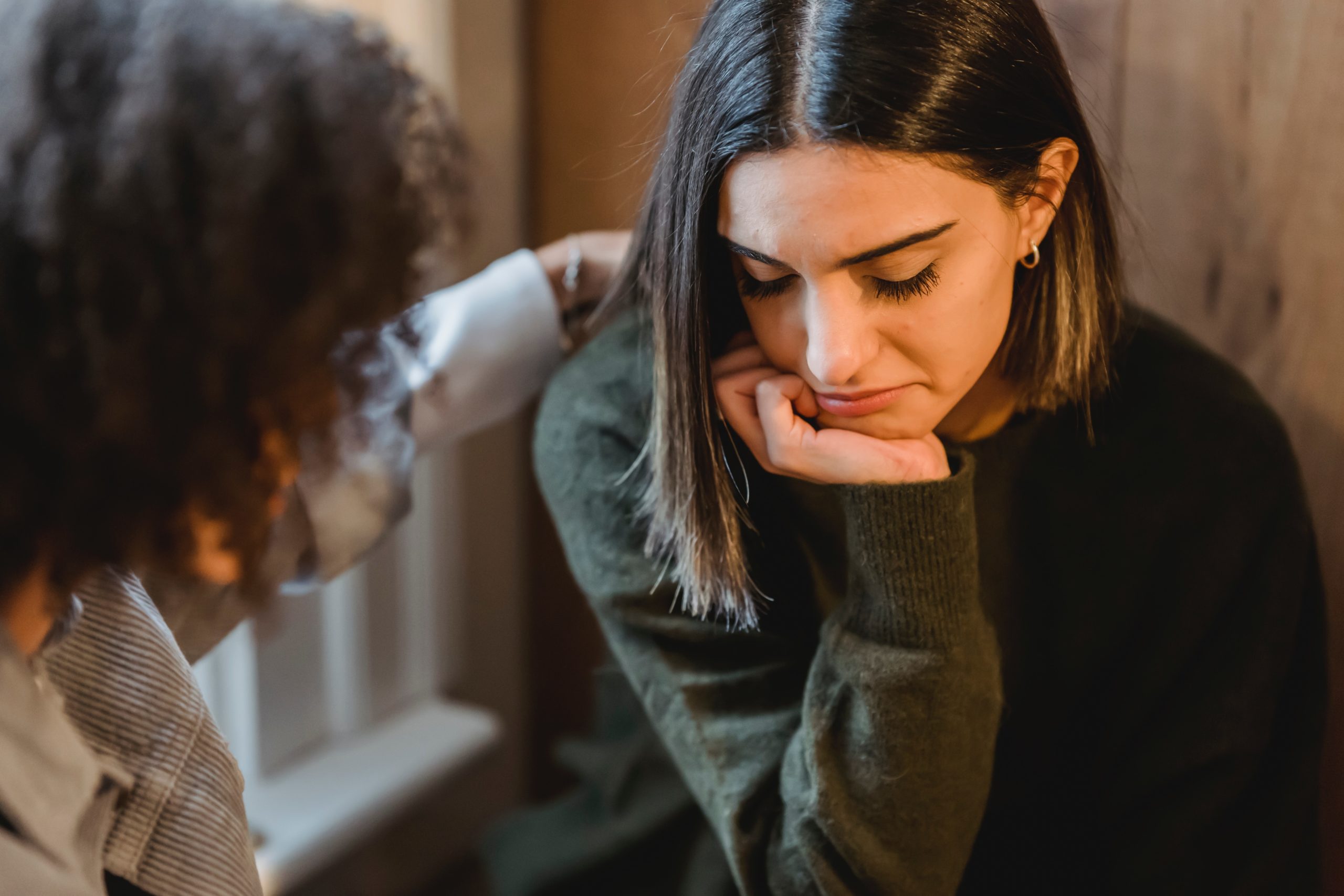 Young woman comforting another young woman who is upset while sitting in a window