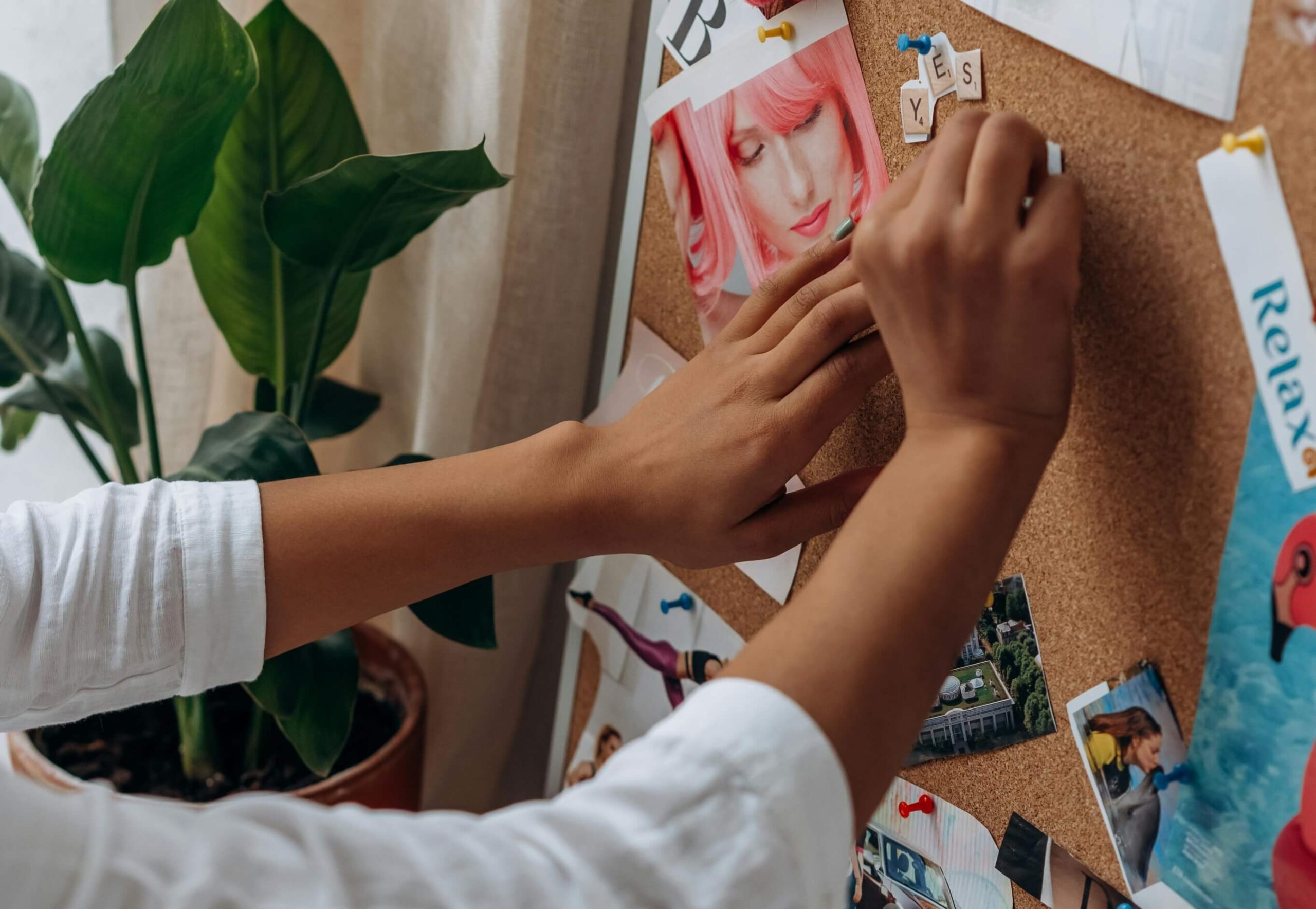 Two hands pin images to a cork board.