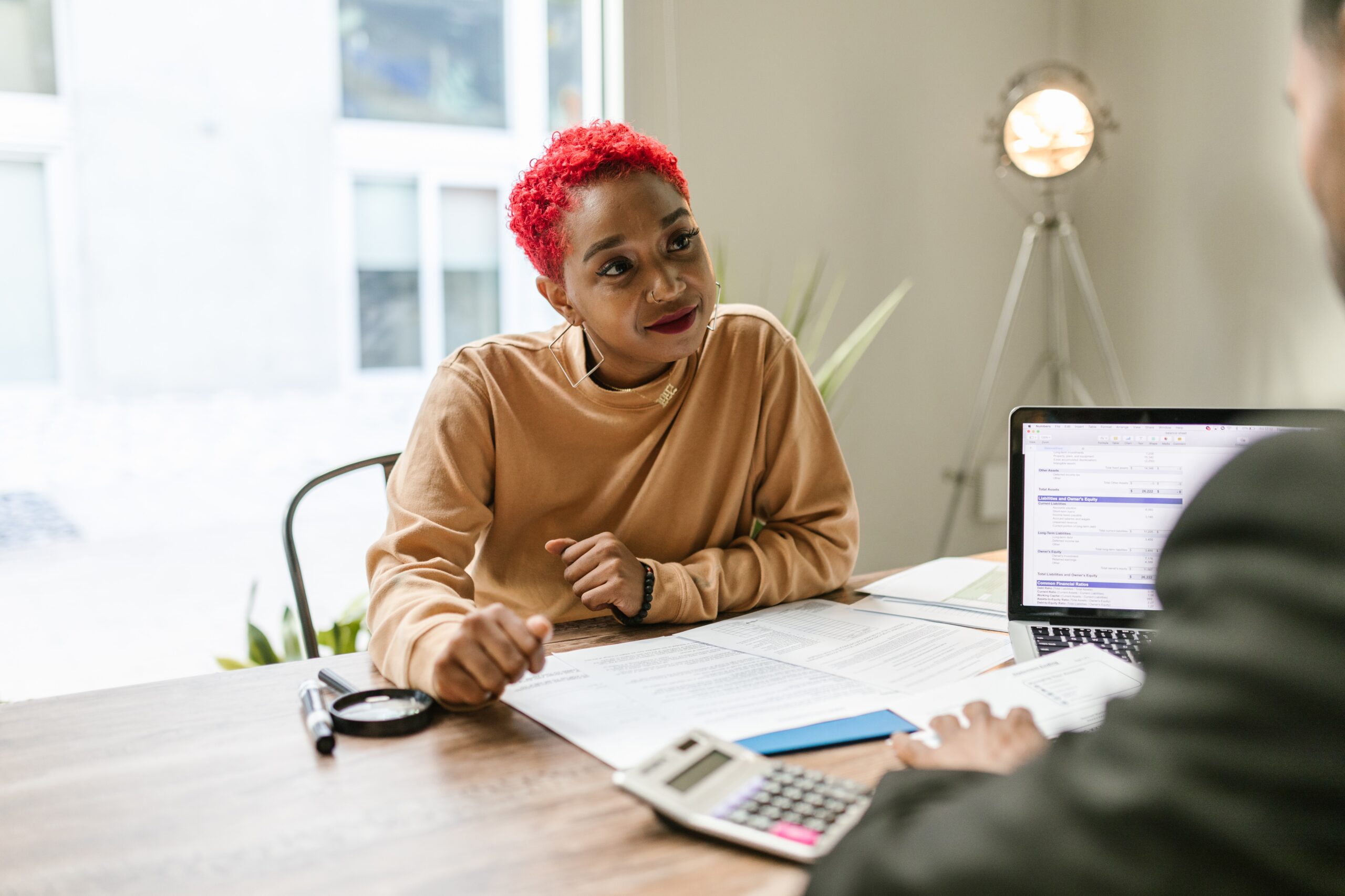 Woman With Short Red Hair Sitting at Desk Reviewing Documents During a Meeting.