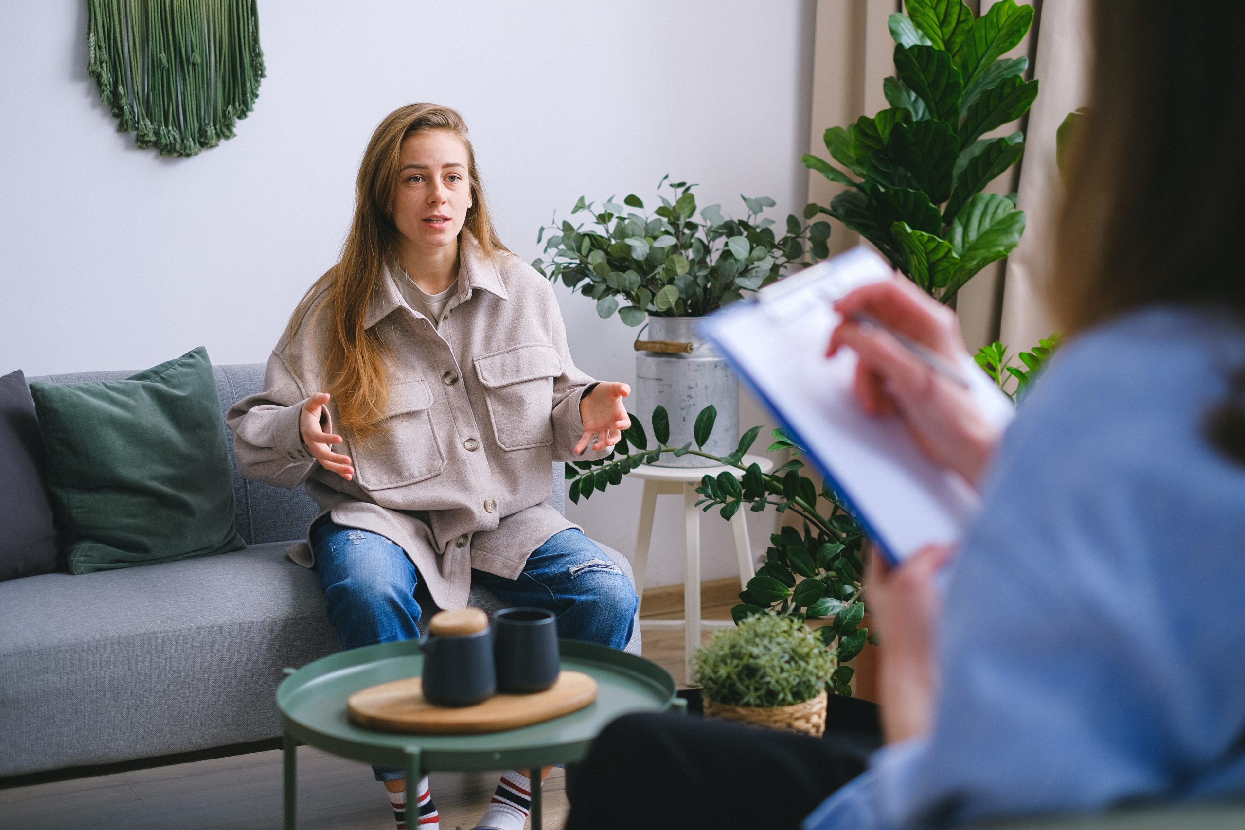 woman sitting on the couch at therapy talking to therapist. Therapist is taking notes. Lots of plants in the room.