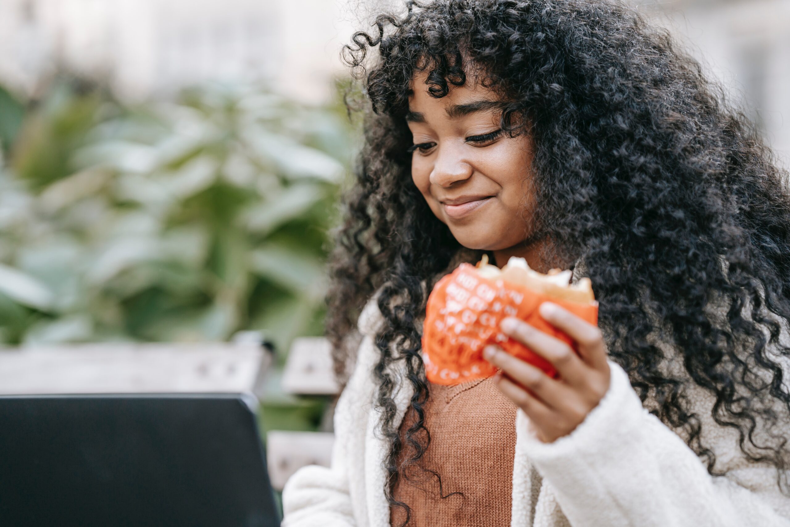 women sitting outdoors eating while on her laptop