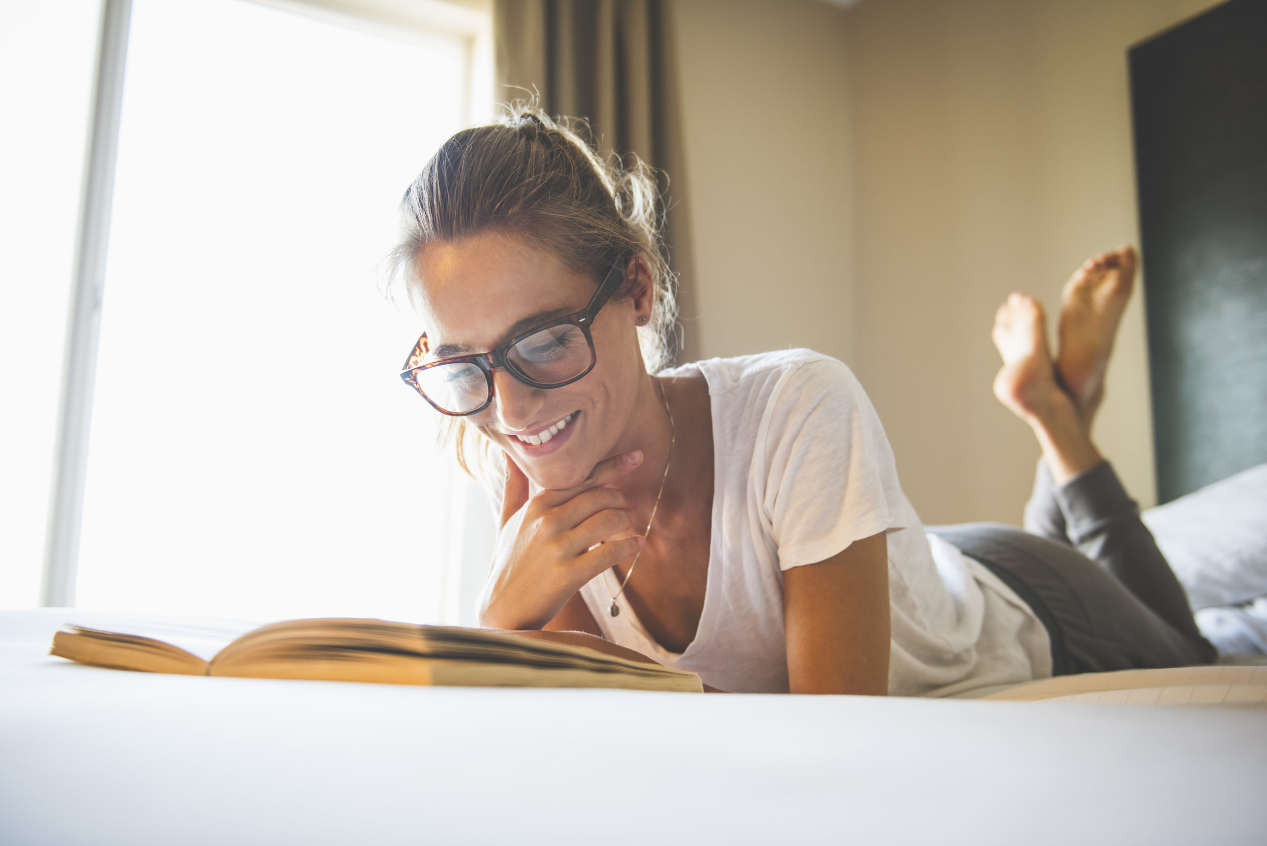 Hispanic woman wearing eyeglasses reading book in bed